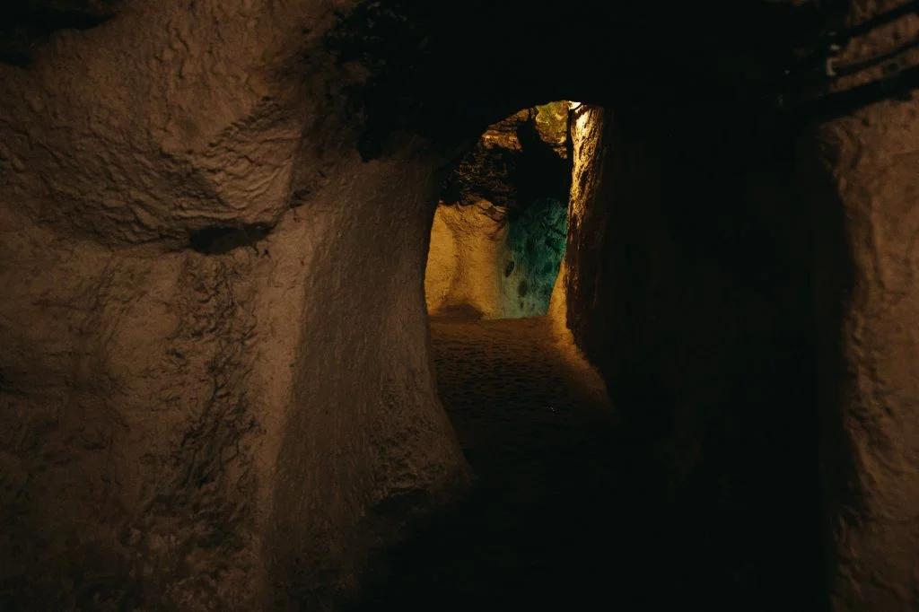 A dark, atmospheric cave tunnel illuminated with a soft light at the far end, suggesting mystery and exploration.
