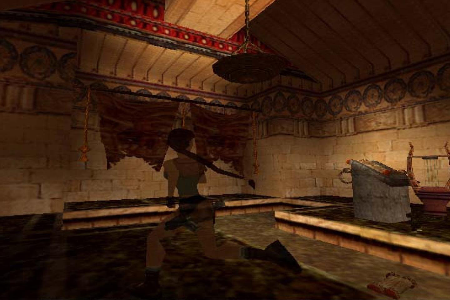 Lara Croft with a shotgun in a temple-like room reflected in the water below.
