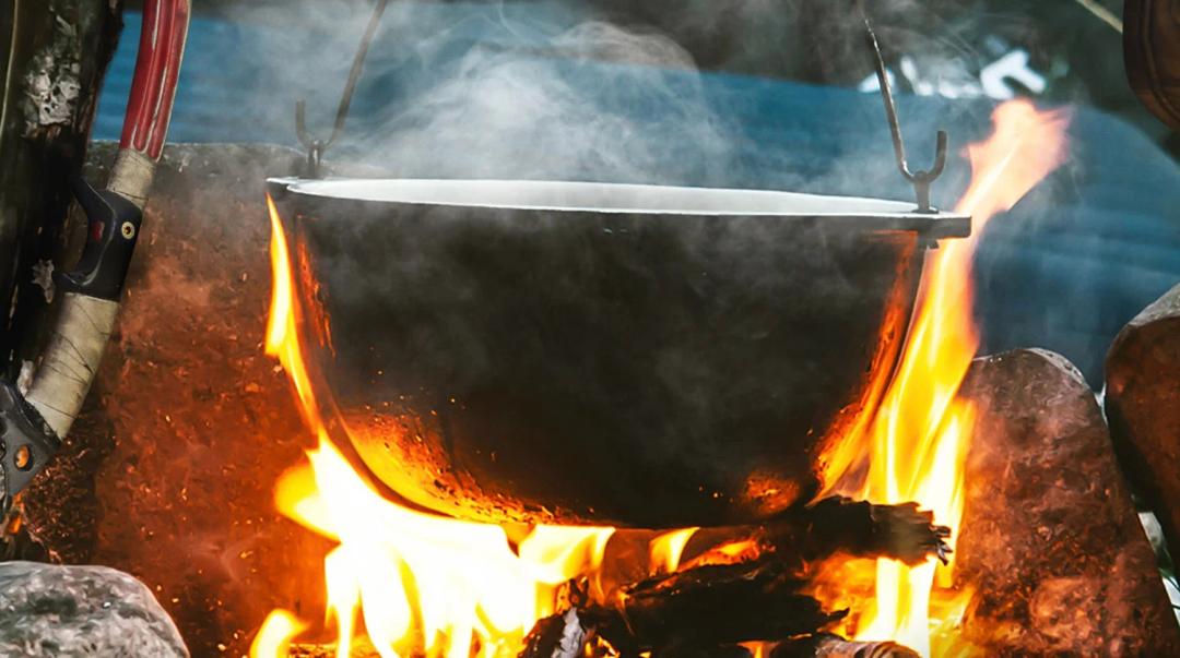 A close-up image of a cauldron over an open fire, hinting at a survival or crafting element within a game.
