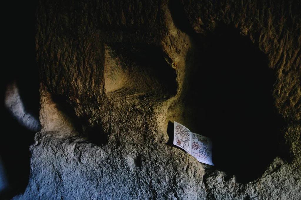 A dimly lit cave with a focus on a rock surface where a card or note with illustrations and text is placed.
