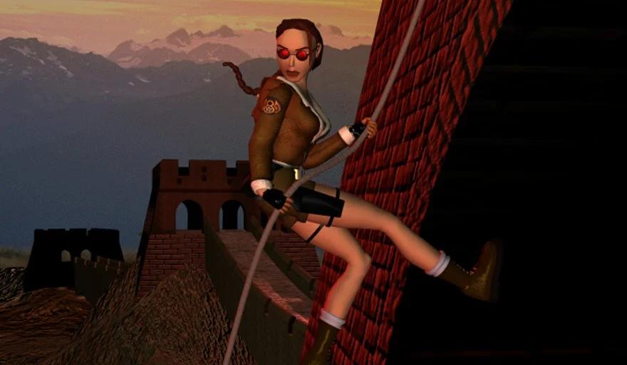 Lara Croft in a leather jacket, scaling a red brick wall with a grappling hook, against a scenic backdrop.