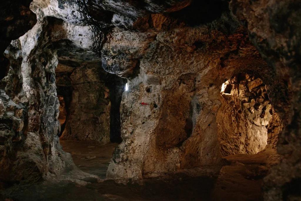 A photo of a naturally lit cave with multiple entrances and a skull-shaped formation on the wall.