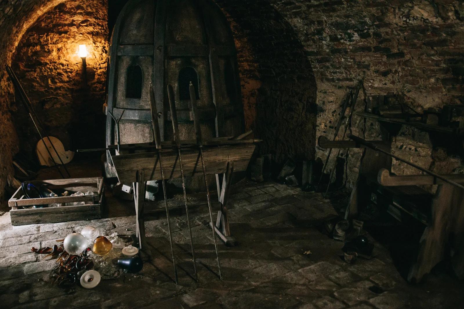 An atmospheric photo of an old, dark workshop with a brick furnace and various tools scattered around.