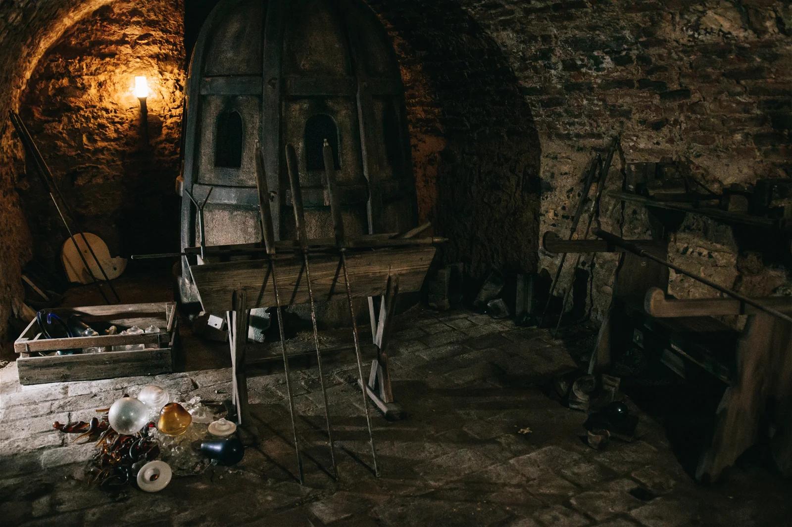 An atmospheric photo of an old, dark workshop with a brick furnace and various tools scattered around.
