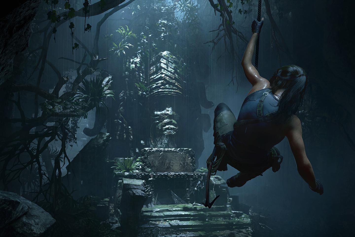 A dramatic screenshot from a Tomb Raider game showing Lara Croft rappelling down into a cavernous temple, illuminated by the ethereal light filtering through the dense jungle above.