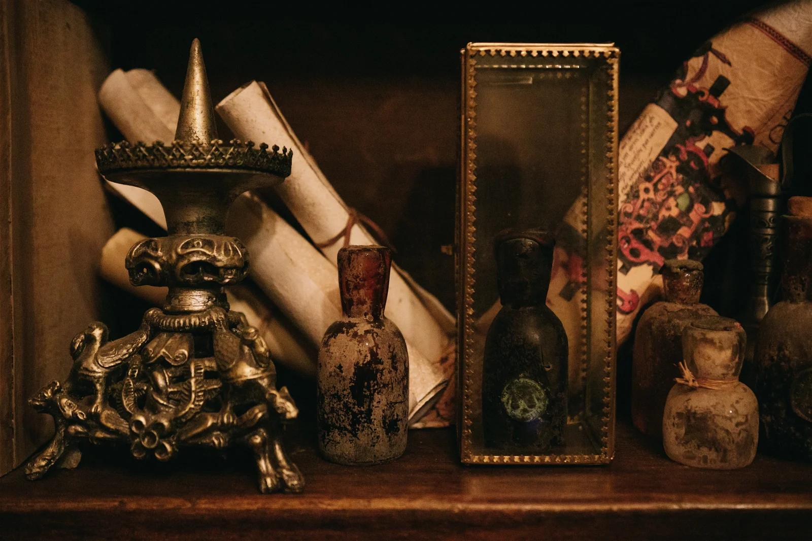 A dimly lit shelf displaying an assortment of ancient-looking artifacts, including scrolls, bottles, and a small statue.