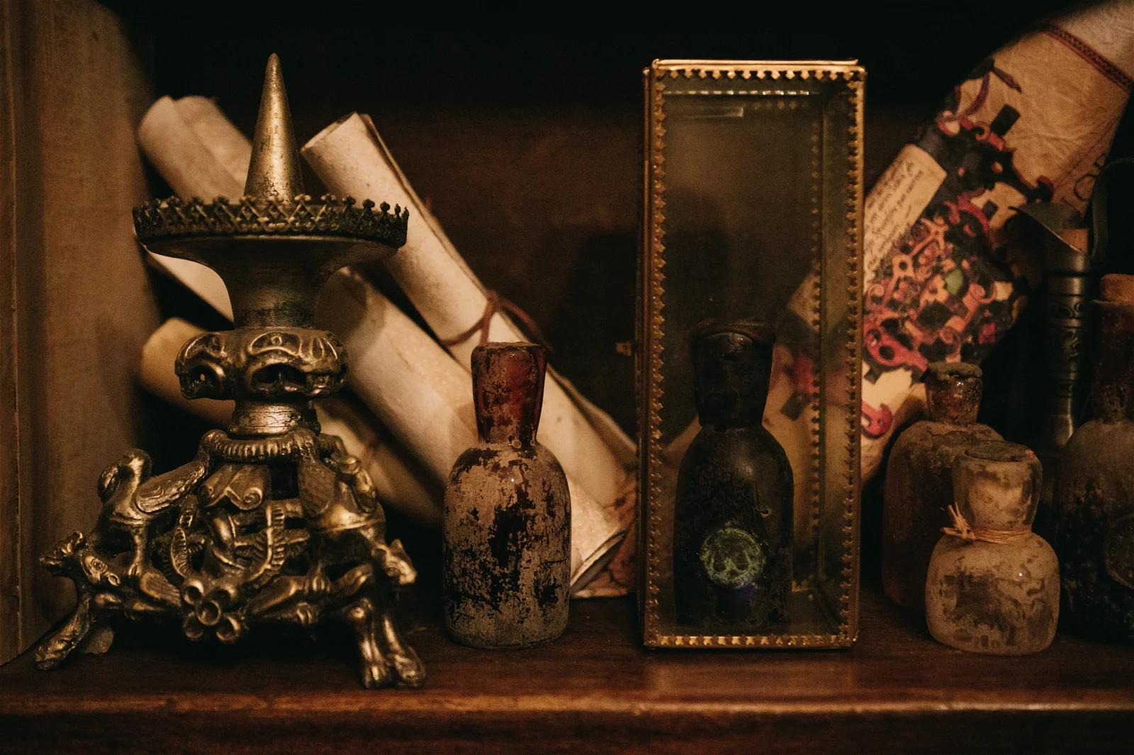 A dimly lit shelf displaying an assortment of ancient-looking artifacts, including scrolls, bottles, and a small statue.
