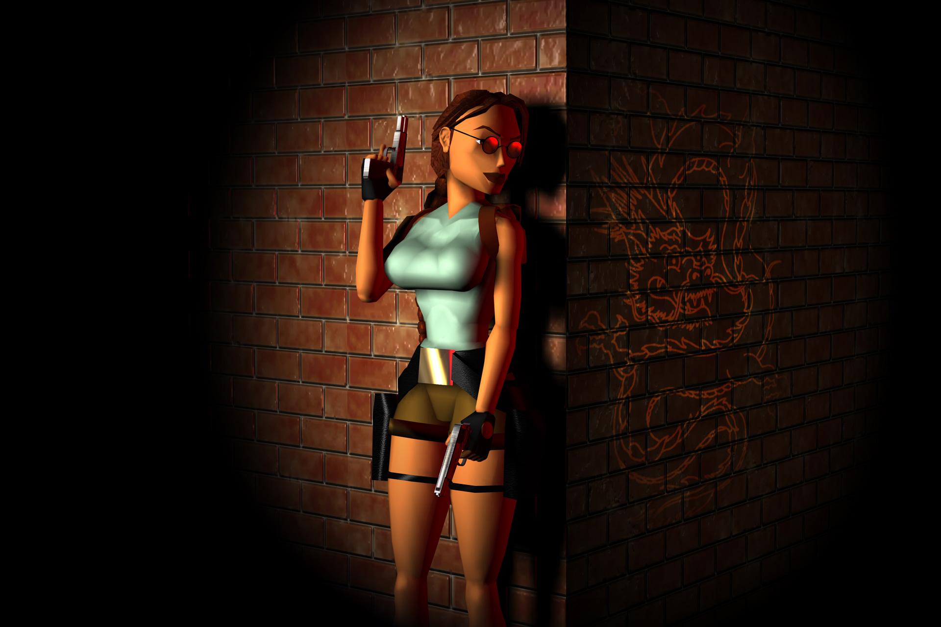 Lara Croft standing against a brick wall with one arm raised. 