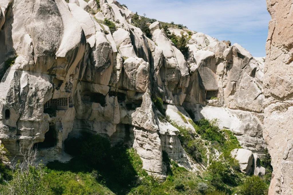 A picturesque view of a rocky landscape with cave dwellings carved into the white, volcanic rock formations.
