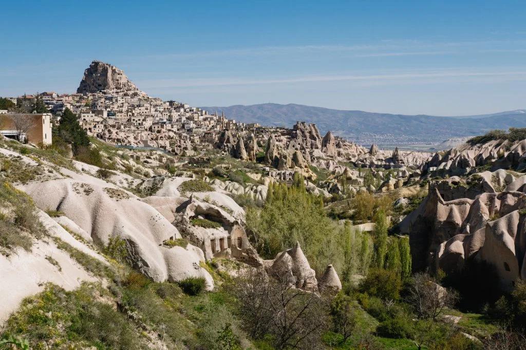 A breathtaking landscape showing a sprawling town atop a hill with unique rock formations surrounding the area.
