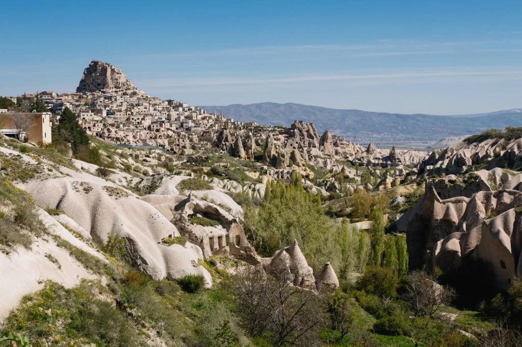 A breathtaking landscape showing a sprawling town atop a hill with unique rock formations surrounding the area.


