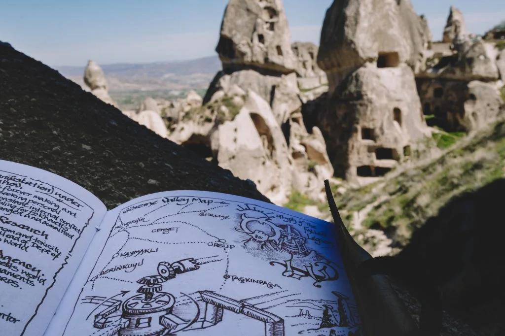 An open notebook with drawings and annotations, set against the backdrop of rocky, pointed formations.
